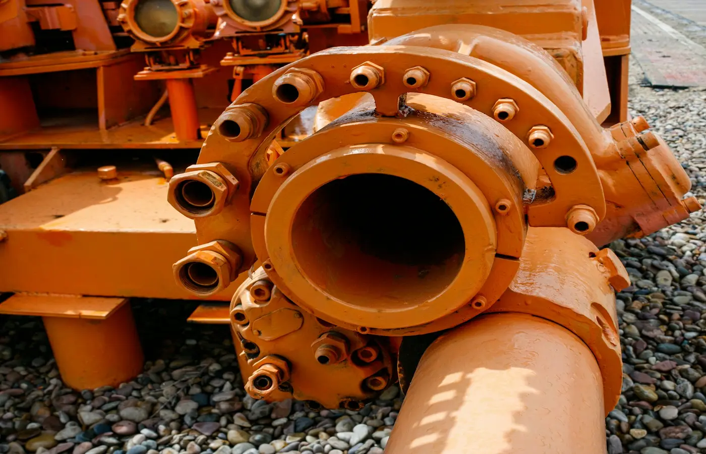 An orange industrial pipe lying on gravel, illustrating slurry transport equipment.